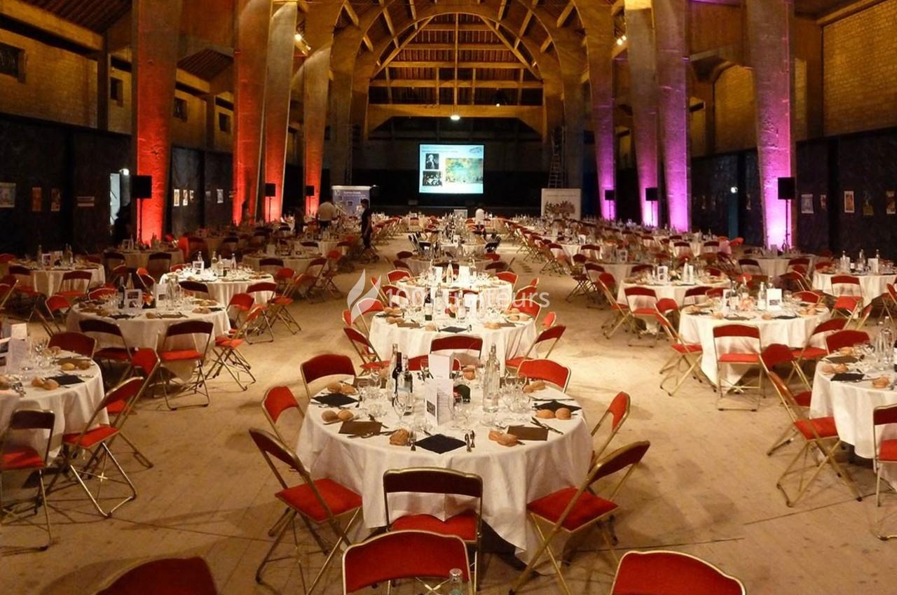 Traiteur Auberge de La Herse Bonneval #1 Salle de réception avec de grandes tables rondes dressées, chaises rouges et éclairage d'ambiance coloré.