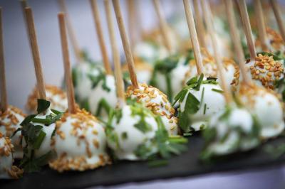 Boules apéritives enrobées de fromage, garnies de graines de sésame et d'herbes fraîches, présentées sur des bâtonnets.