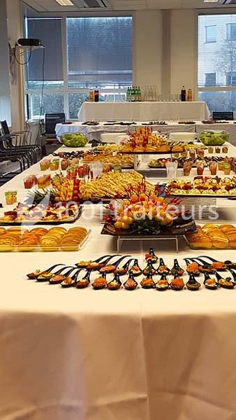 Buffet varié avec plats salés et sucrés disposés sur plusieurs tables dans une salle lumineuse.