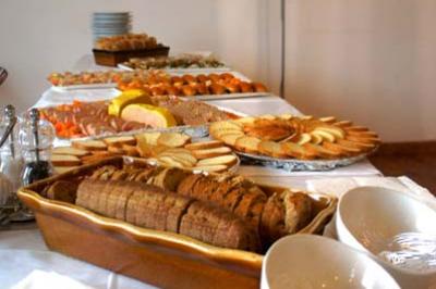 Traiteur Vb Traiteur Gradignan #5 Buffet avec pain tranché, biscuits, fruits et plats variés disposés sur une table blanche éclairée par une lampe.