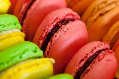 Macarons Macarons colorés alignés de près, avec des nuances de rose, jaune et vert, garnis d'une crème au centre.
