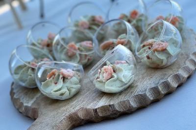 Verrines rondes contenant une mousse verte garnie de crevettes, présentées sur une planche en bois.