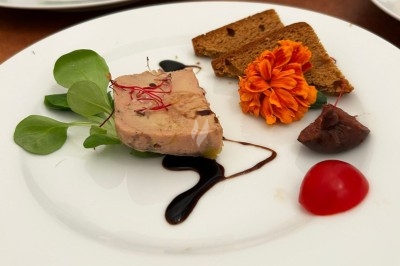 Assiette de foie gras avec pain, fleur comestible, réduction balsamique, tomate cerise et garniture verte.