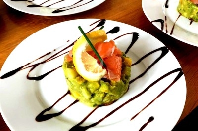 Assiette de tartare d'avocat et saumon fumé, décorée de citron, ciboulette et filet de sauce balsamique.