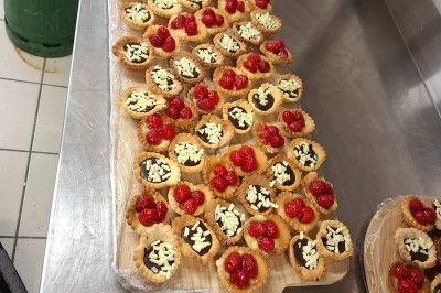 Plateau de tartelettes garnies de chocolat, éclats de chocolat blanc et framboises, disposé sur un plan de travail en…
