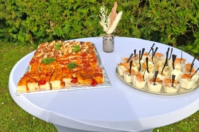 Plateau de bouchées salées et verrines disposé sur une table blanche en extérieur, avec un vase décoratif.