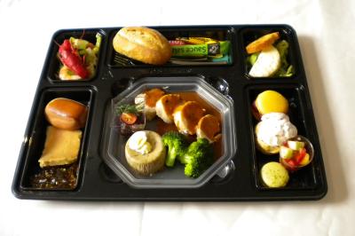 Plateau-repas composé de viande en sauce, légumes, fromage, pain, dessert et condiments, présenté sur un plateau…