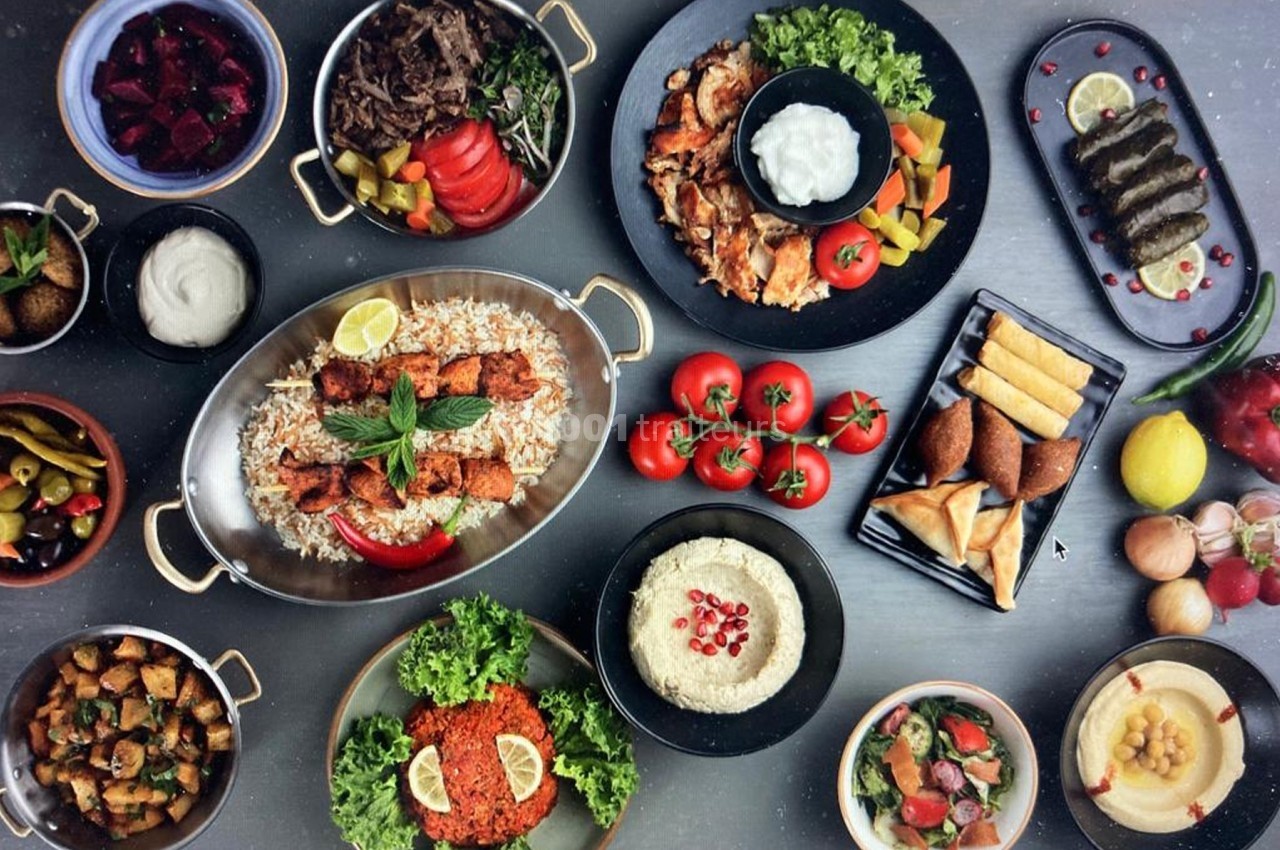 Assortiment de plats méditerranéens variés avec viandes, légumes, mezzés, pains et sauces, disposés sur une table.