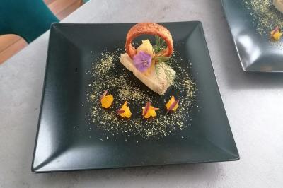Dessert dressé sur une assiette noire, avec mousse, fleurs comestibles, croustillant et décorations colorées.