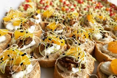 Assortiment de canapés garnis de fromage frais, noix, morceaux de fruits et pousses, disposés sur un plateau.