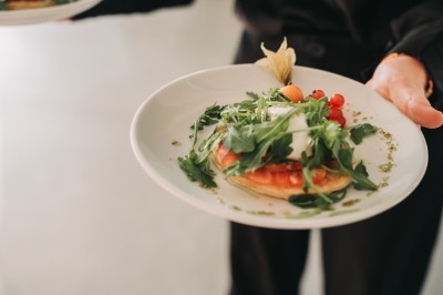 Assiette garnie d'une salade de roquette, tomates cerises, fromage et une base croustillante, tenue par une personne.