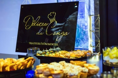 Buffet varié avec des plats salés et sucrés devant un panneau ’Délices du Congo, traiteur événementiel’.