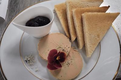 Assiette avec deux tranches de foie gras, une fleur comestible, du sel, des toasts triangulaires et un ramequin de confiture.