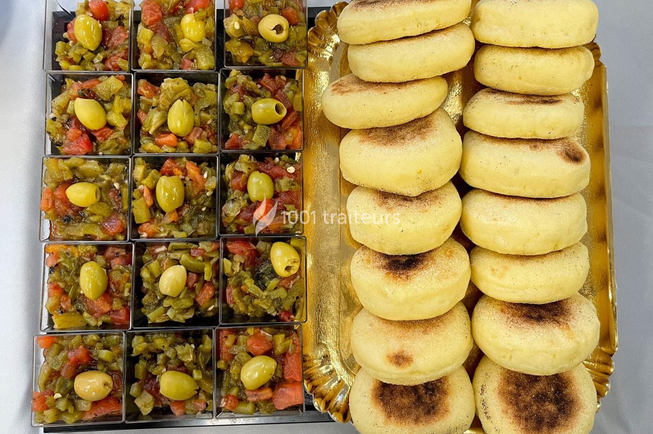 Traiteur Dihya Marseille 13 #1 Plateau avec des mini bols de salade de légumes garnis d'olives vertes et des pains ronds dorés empilés.