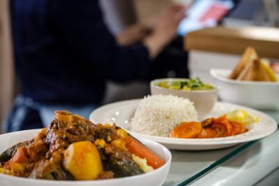 Traiteur Dihya Marseille 13 #3 Assiette de couscous avec légumes et viande, accompagnée de riz, carottes et sauce, en arrière-plan une personne floue.