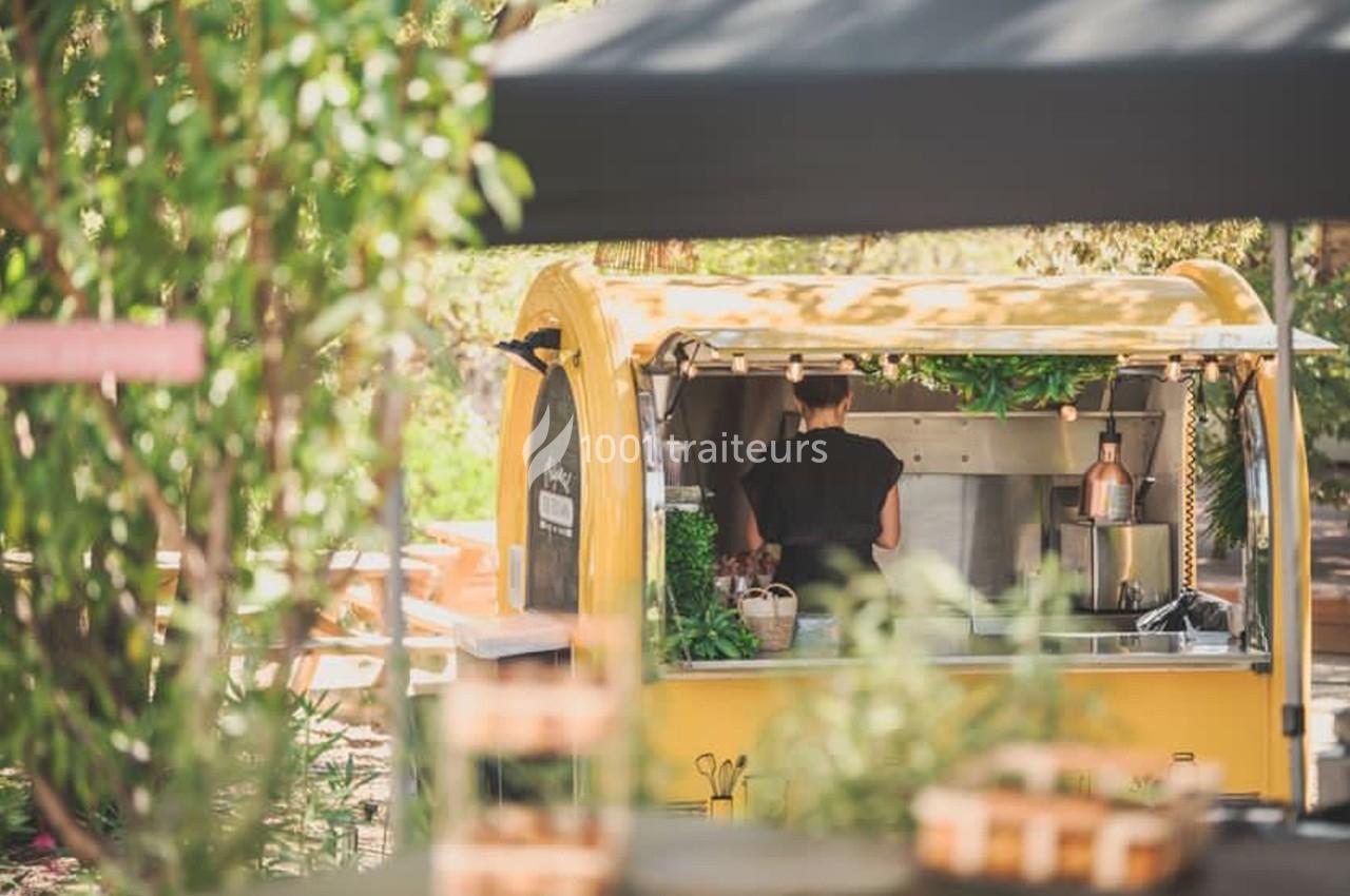 Traiteur Ben’s Traiteur By Original Food Truck Mania Saint-Laurent-du-Var #1 Un food truck jaune dans un cadre extérieur verdoyant, avec une personne préparant des plats à l'intérieur.