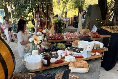 Traiteur Ben’s Traiteur By Original Food Truck Mania Saint-Laurent-du-Var #2 Plateau de fromages, charcuteries et pains sur une table en extérieur, avec des musiciens en arrière-plan.