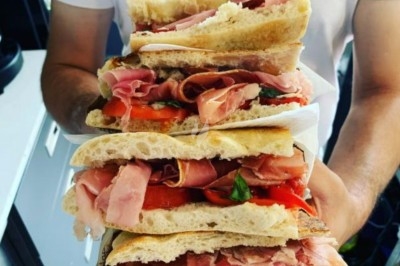 Sandwichs garnis de jambon, tomates et basilic, empilés et tenus à deux mains.