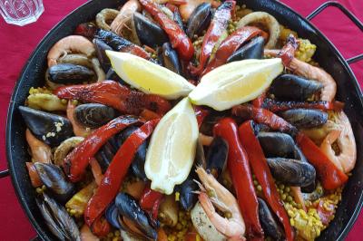 Traiteur Comptoir des Saveurs  Saint-Martin-d'Uriage #2 Plat de paella avec fruits de mer, poivrons rouges grillés et quartiers de citron disposés sur un fond rouge.