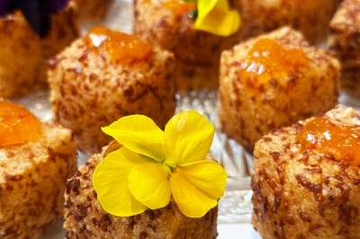 Petits gâteaux dorés garnis de confiture d'orange et décorés de fleurs jaunes comestibles sur un plateau en verre.