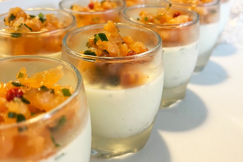 Verrines de panna cotta salée garnies de tartare de saumon et herbes fraîches, présentées sur une table blanche.