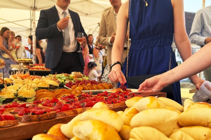 Buffet en plein air avec des invités se servant parmi des plats variés, incluant pains, viennoiseries et amuse-bouches.