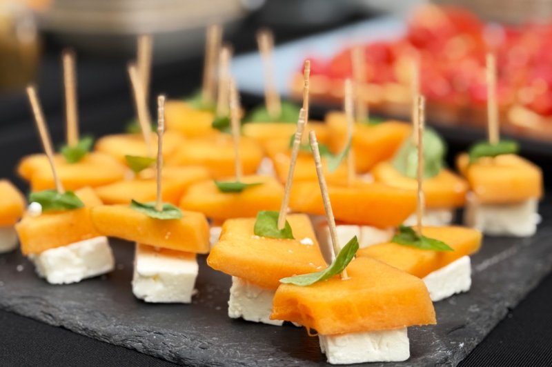 Bouchées apéritives composées de cubes de feta, morceaux de melon et feuilles de basilic, présentées sur un plateau ardoise.