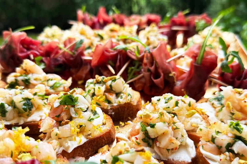 Assortiment de tapas avec toasts garnis de crevettes et herbes fraîches, accompagnés de roulés de jambon cru.