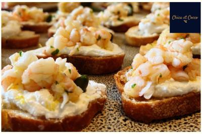 Des pièces faites maison  Tranches de pain garnies de fromage frais, crevettes et herbes, disposées sur une surface mouchetée.