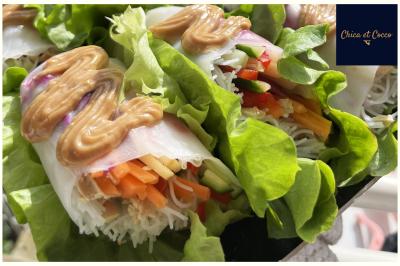Une cuisine du monde Rouleaux de printemps garnis de légumes colorés, nouilles et sauce cacahuète, présentés sur des feuilles de salade.