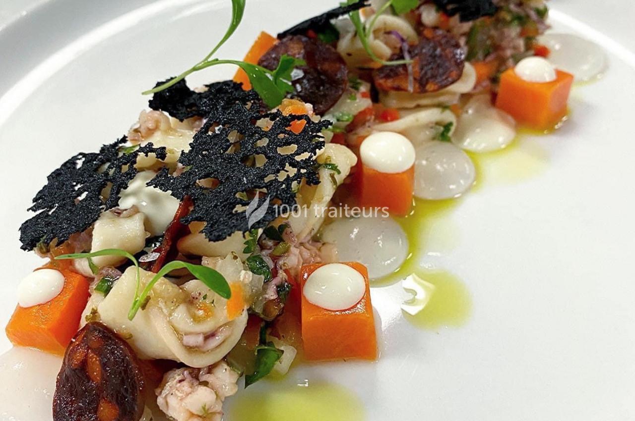 Assiette gastronomique avec présentation soignée de légumes, fruits de mer, tuiles noires et touches de sauce.