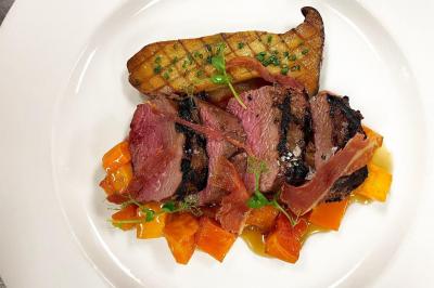 Assiette garnie de magret de canard, légumes rôtis et chips de peau croustillante, présentée avec soin.