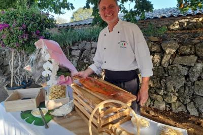 Chef souriant présentant un filet de saumon fumé et des accompagnements sur une table en extérieur.