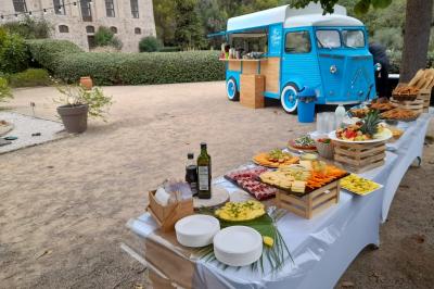 Table dressée avec des plats variés et un food truck bleu en arrière-plan dans un jardin.