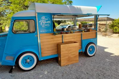 food truck Camion bleu aménagé en food truck avec comptoir en bois, stationné sur un sol gravillonné près d'arbres.