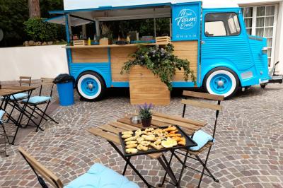food truck mobilier terrasse Camion bleu aménagé en food truck, stationné sur une place pavée avec tables et plateau de snacks en premier plan.