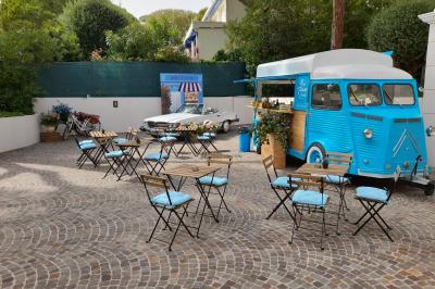 food truck mobilier terrasse Camion bleu aménagé en food truck avec tables et chaises sur une terrasse pavée, voiture blanche en arrière-plan.