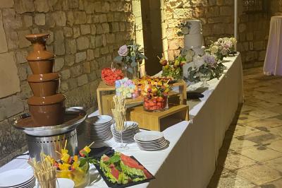 Traiteur Boeuf Traiteur Nice #2 Buffet avec fontaine de chocolat, brochettes de fruits, gâteaux décorés et assiettes sur une table dans un cadre en pierre.