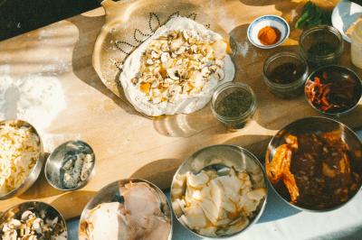 Traiteur Pizzaiolo Tsogani Paris #5 Ingrédients variés et pâte à pizza garnie de champignons disposés sur une table en bois.