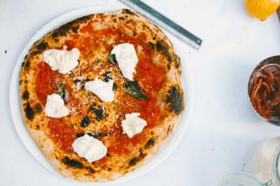 Traiteur Pizzaiolo Tsogani Paris #4 Pizza napolitaine garnie de sauce tomate, mozzarella, basilic et fromage râpé, servie sur une assiette blanche.