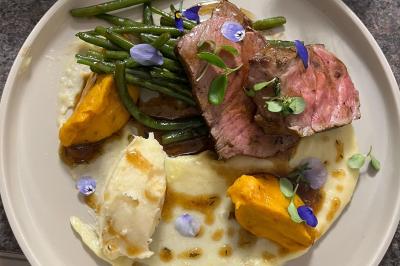 Assiette garnie de viande rosée, haricots verts, purées de pommes de terre et de patate douce, décorée de fleurs comestibles.