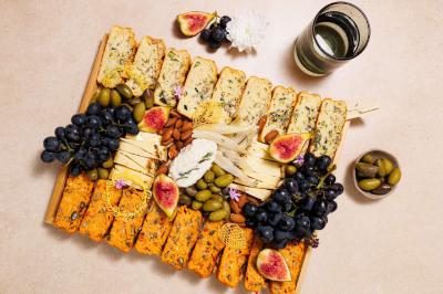 Plateau de fromages variés avec figues, raisins, olives, amandes et pain, accompagné d'un verre de vin blanc.
