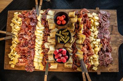 Planche Plateau en bois garni de charcuteries, fromages, cornichons, tomates cerises et radis, avec des couteaux disposés.