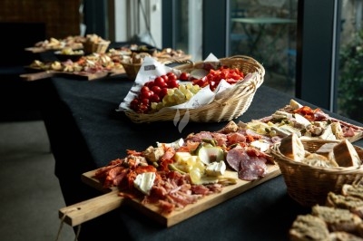Planche Plateaux de charcuterie, fromages et pains disposés sur une table avec des paniers de fruits et légumes en arrière-plan.