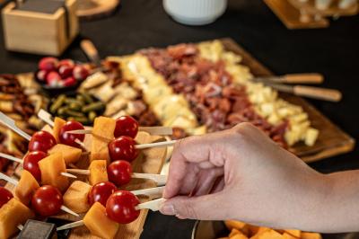 Planche Main prenant une brochette de tomates cerises et melon sur un buffet composé de charcuterie, fromages et fruits.