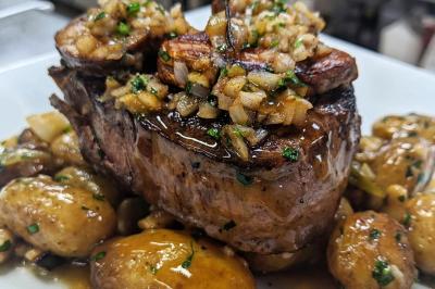 Plat de viande grillée garnie d'oignons et herbes, accompagné de pommes de terre rôties nappées de sauce.