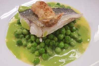 Filet de poisson avec peau grillée, posé sur des petits pois et une sauce verte, garni d'une langoustine.