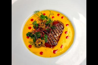 Traiteur Jsch Prestations Culinaires Nanterre #5 Plat gastronomique composé d'un morceau de viande grillée, sauce jaune, herbes fraîches et fleurs comestibles.