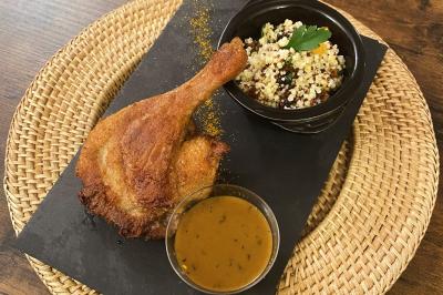 Cuisse de poulet rôtie servie avec une sauce, du quinoa aux herbes et légumes, présentée sur une ardoise noire.