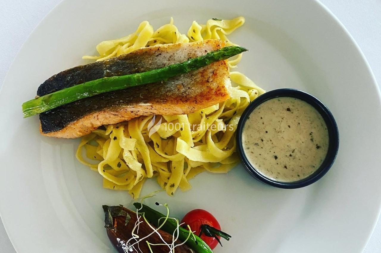 Assiette contenant un filet de saumon grillé sur des tagliatelles, une sauce en bol, et des légumes grillés.